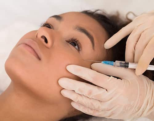 A woman receives a biostimulating cosmetic filler injection between the eye and the temple