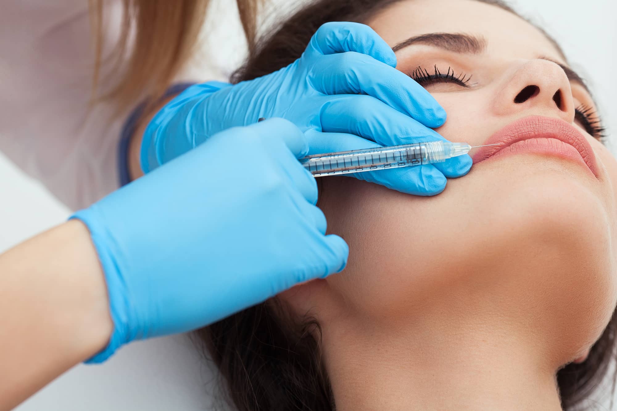 the doctor inject a filler into the woman`s lip